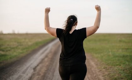 A woman with her back to the camera standing with a field with her arms raised 